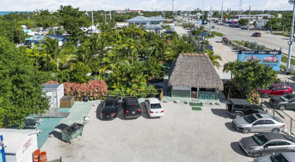 Outdoor Attractions in Marathon FL featuring tropical palm trees, tiki-style hut, mini golf area, and parking at Porky’s Bayside Restaurant and Marina along the scenic Gulfside roadway.